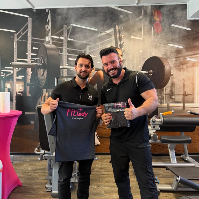 Zwei Männer in Sportkleidung, lächelnd und posierend in einem Fitnessstudio.